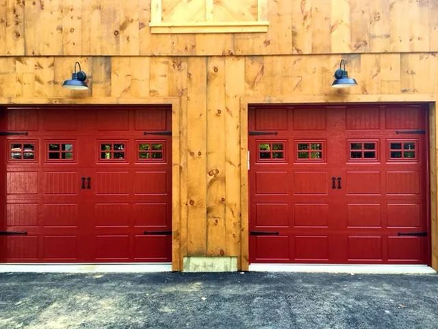 Two red garage doors in a wooden building facade with blue lamps above them
