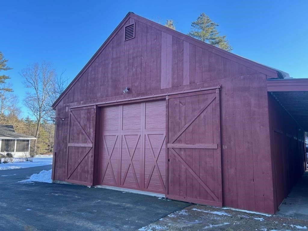 Red barn with large double doors on a snowy driveway under a clear blue sky