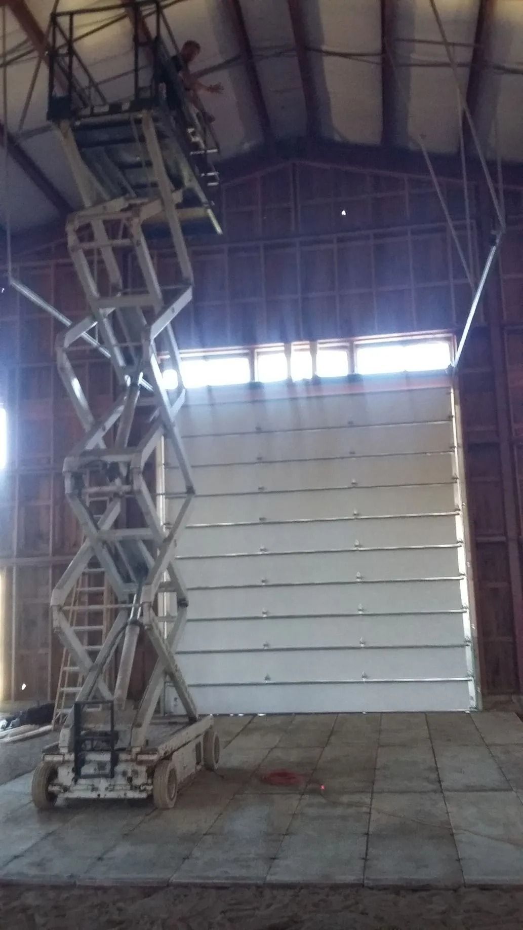 Scissor lift raised inside a warehouse, reaching a tall white wall or door panel.