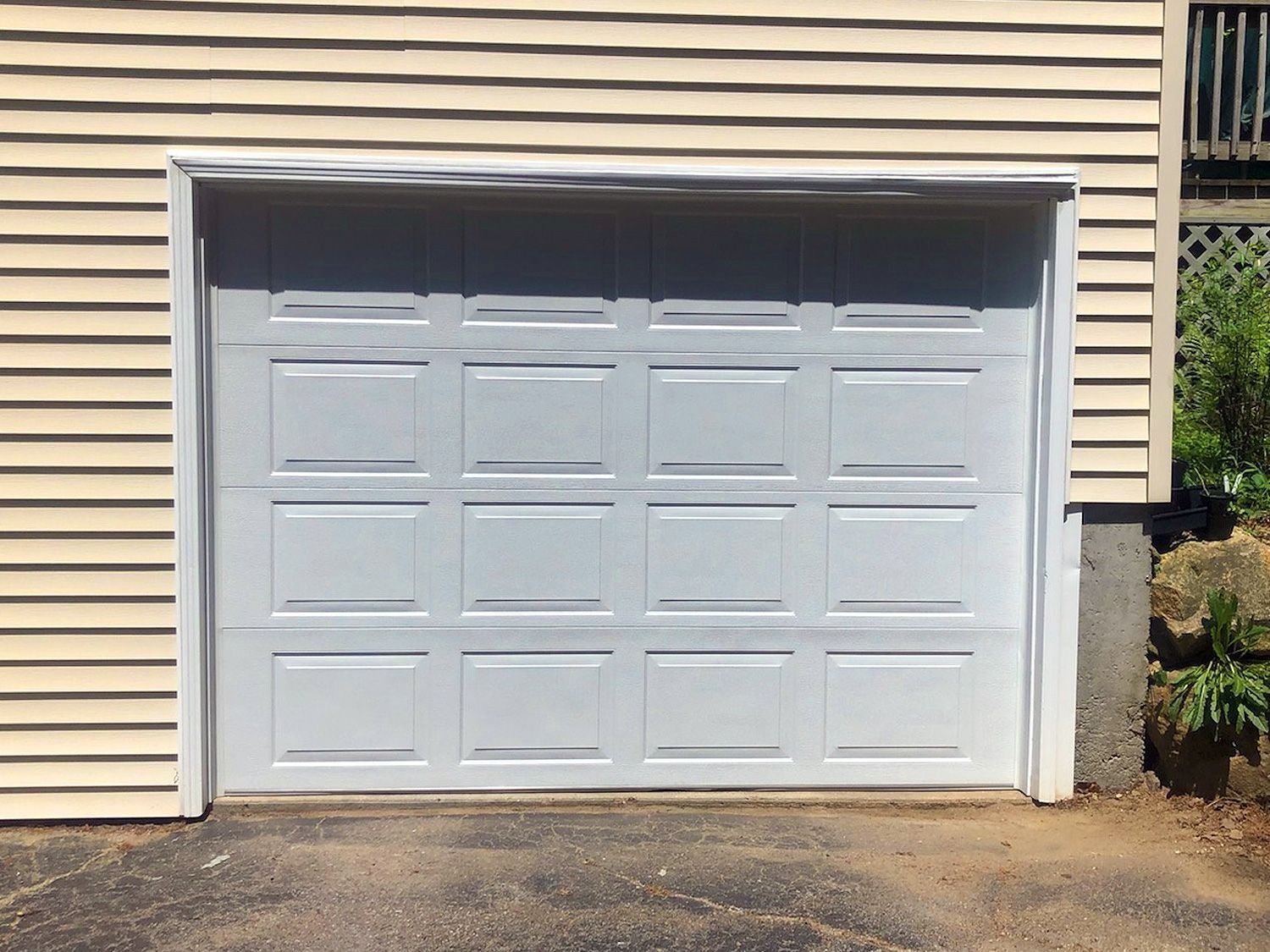 White paneled garage door on a beige house exterior with concrete driveway.
