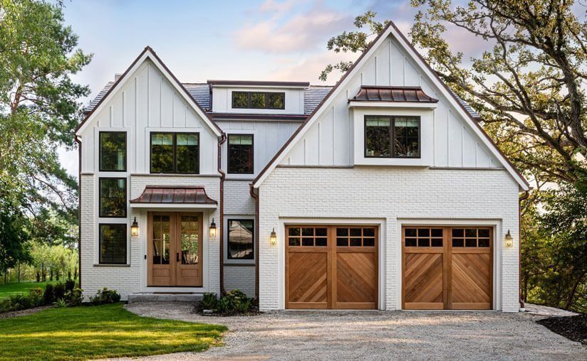 Modern white house with dark trim, wooden garage doors, and a front entrance beneath trees.