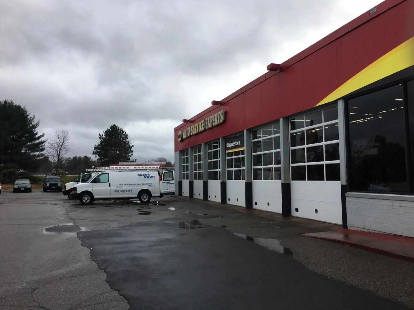 Rainy parking lot outside a red-roofed storefront with service vans parked by the entrance