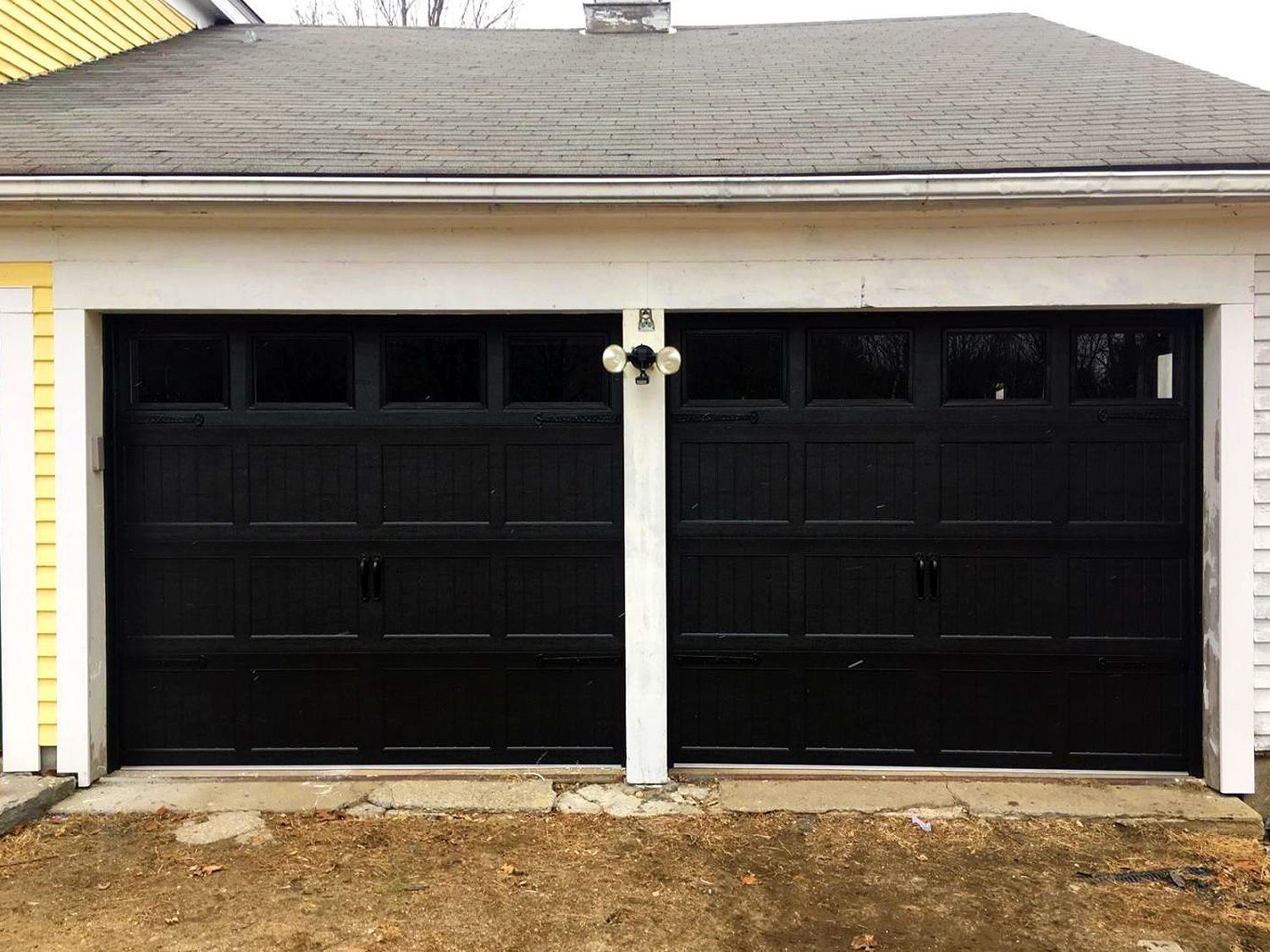 Two black garage doors with small windows on a beige house exterior