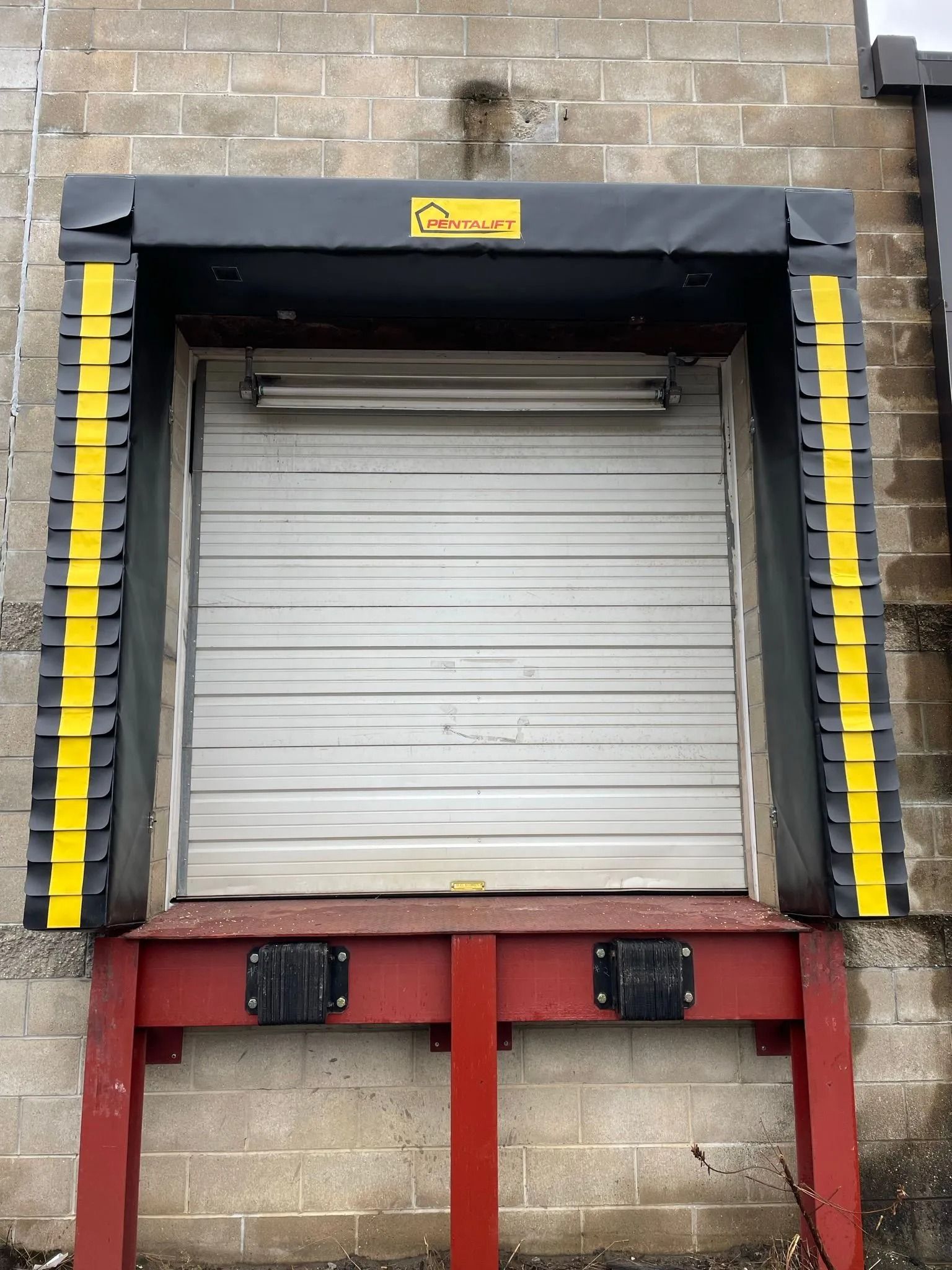 Closed white loading dock door framed in black and yellow safety bumpers against a brick wall.