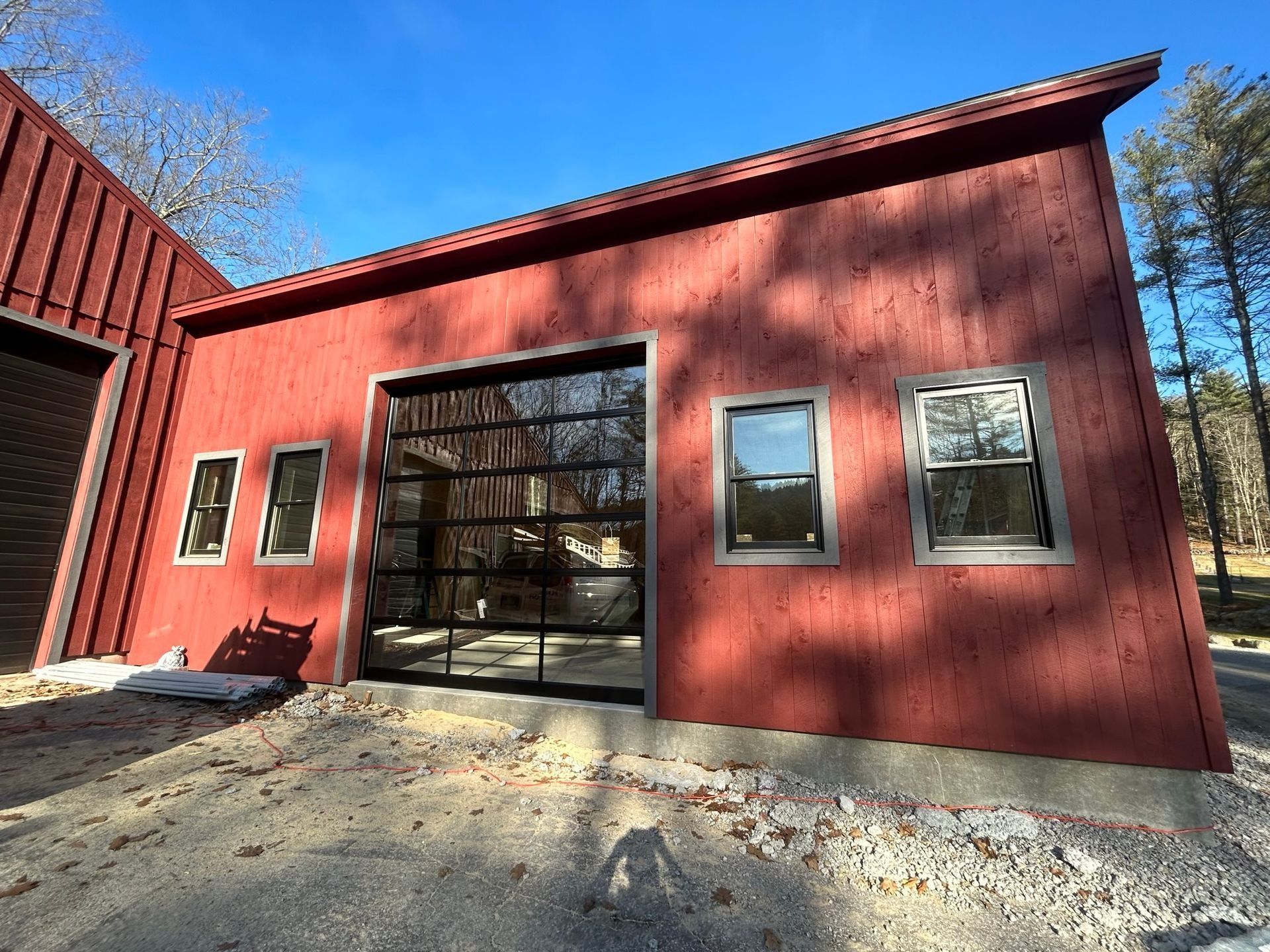 Red building with black garage door and windows, viewed from a sunlit gravel driveway.