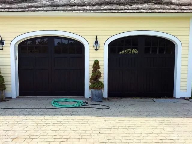 Two dark garage doors in a yellow house exterior, with a hose on the driveway.