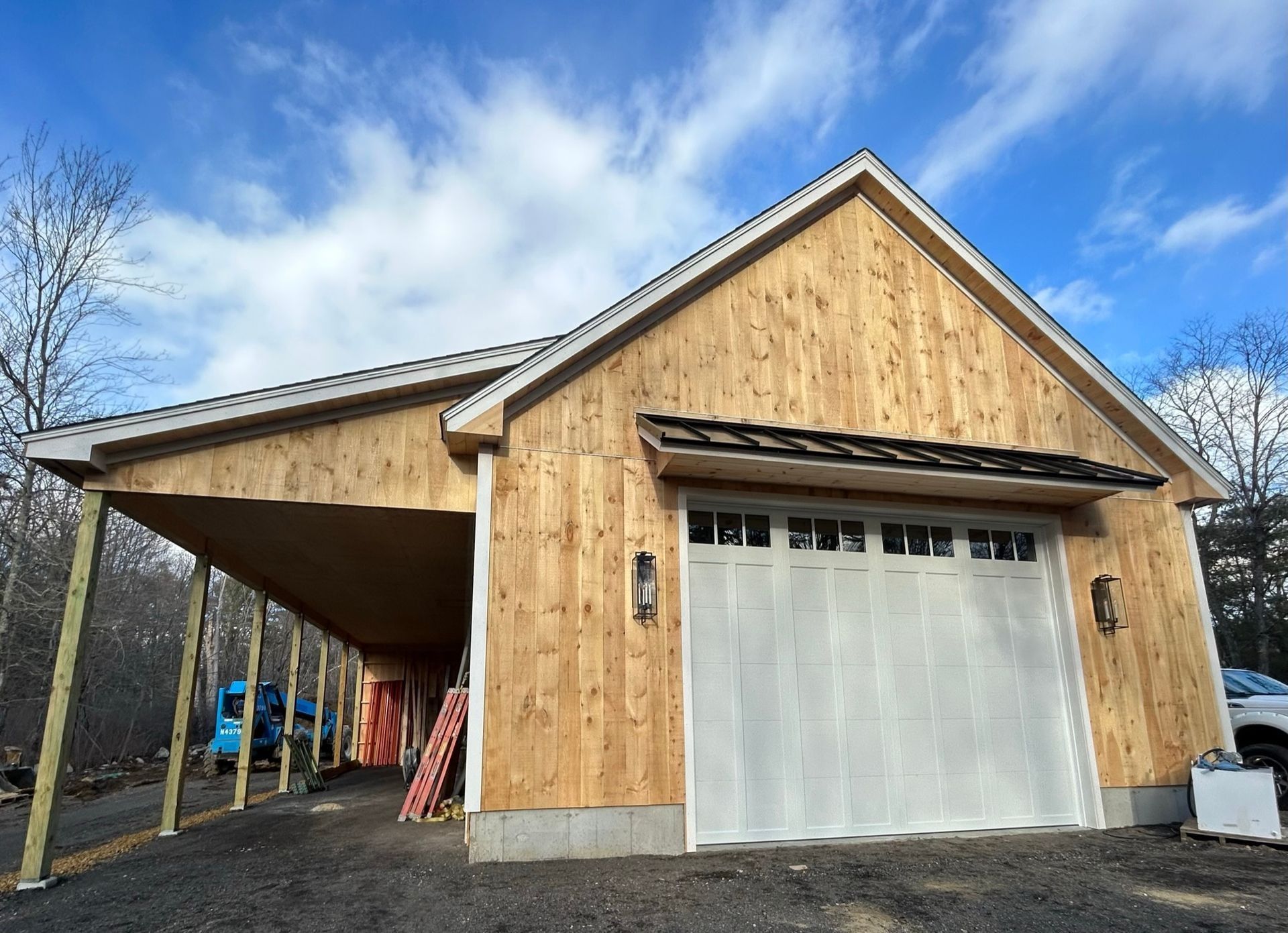 Wooden garage with a gray door and covered side storage area under a peaked roof