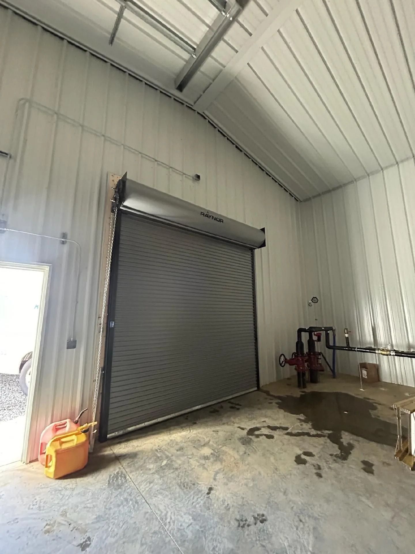 Industrial garage interior with a closed roll-up door, concrete floor, and cleaning supplies against white walls