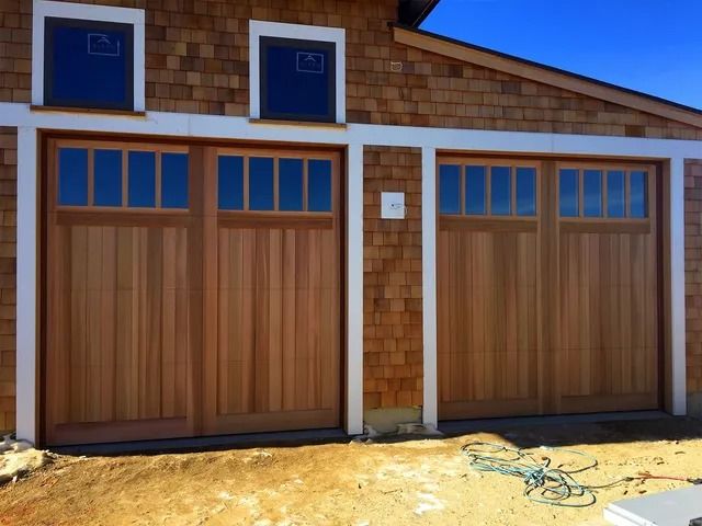 Two wooden garage doors on a tan shingled building with blue trim and small upper windows