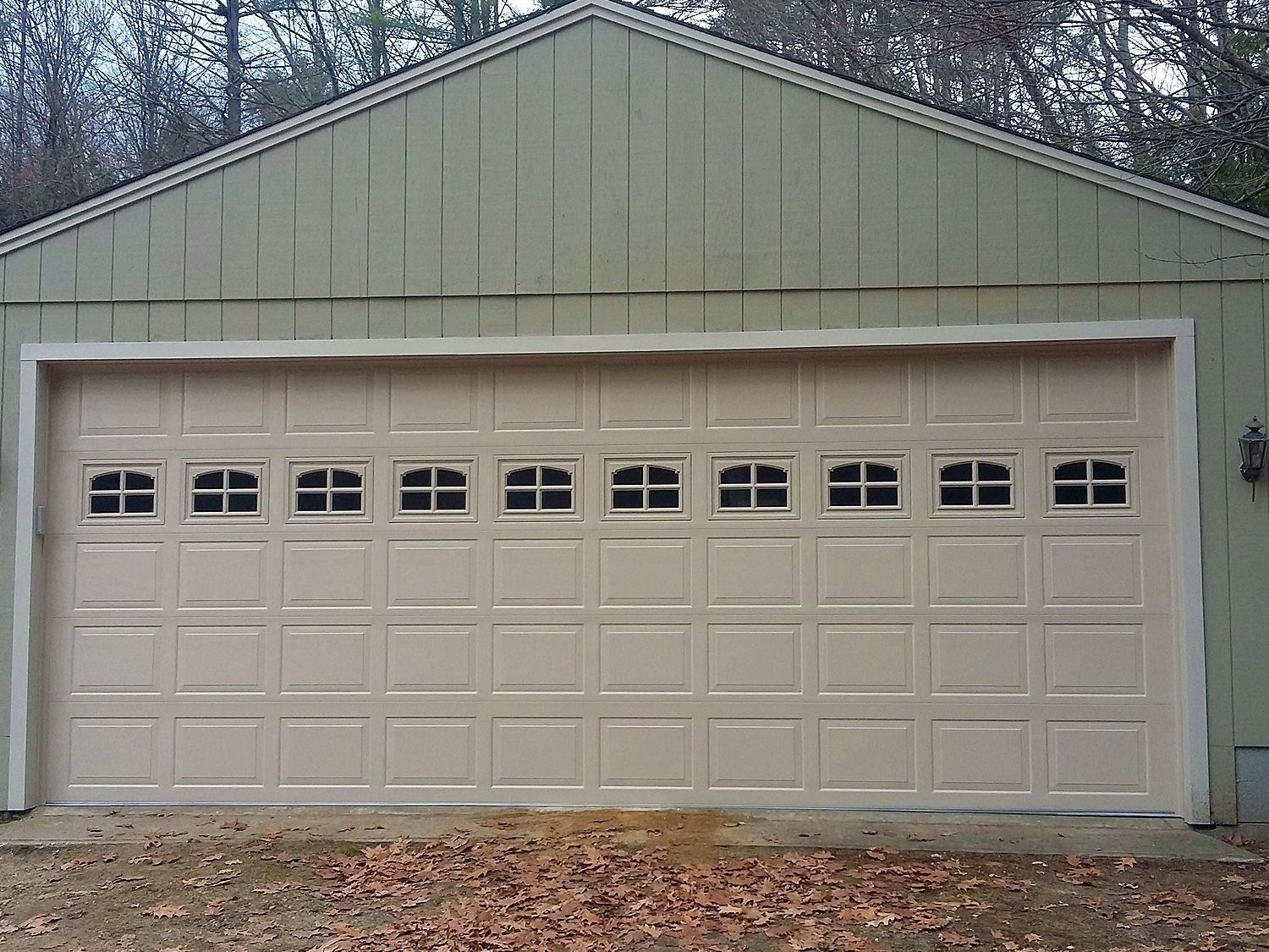Beige two-car garage with white double doors and small windows under a green gable roof.