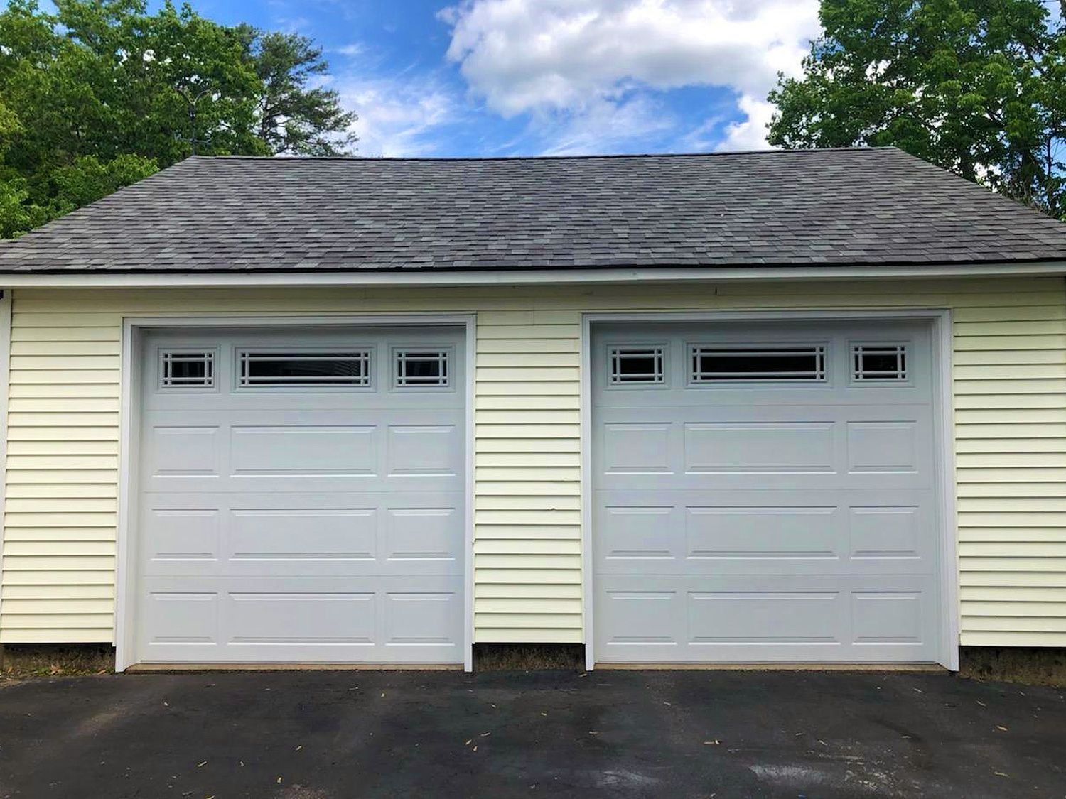 Two white garage doors on a beige house with gray shingled roof and blue sky above