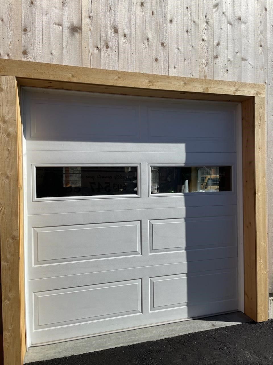 White garage door with four windows set in a wood-sided wall.