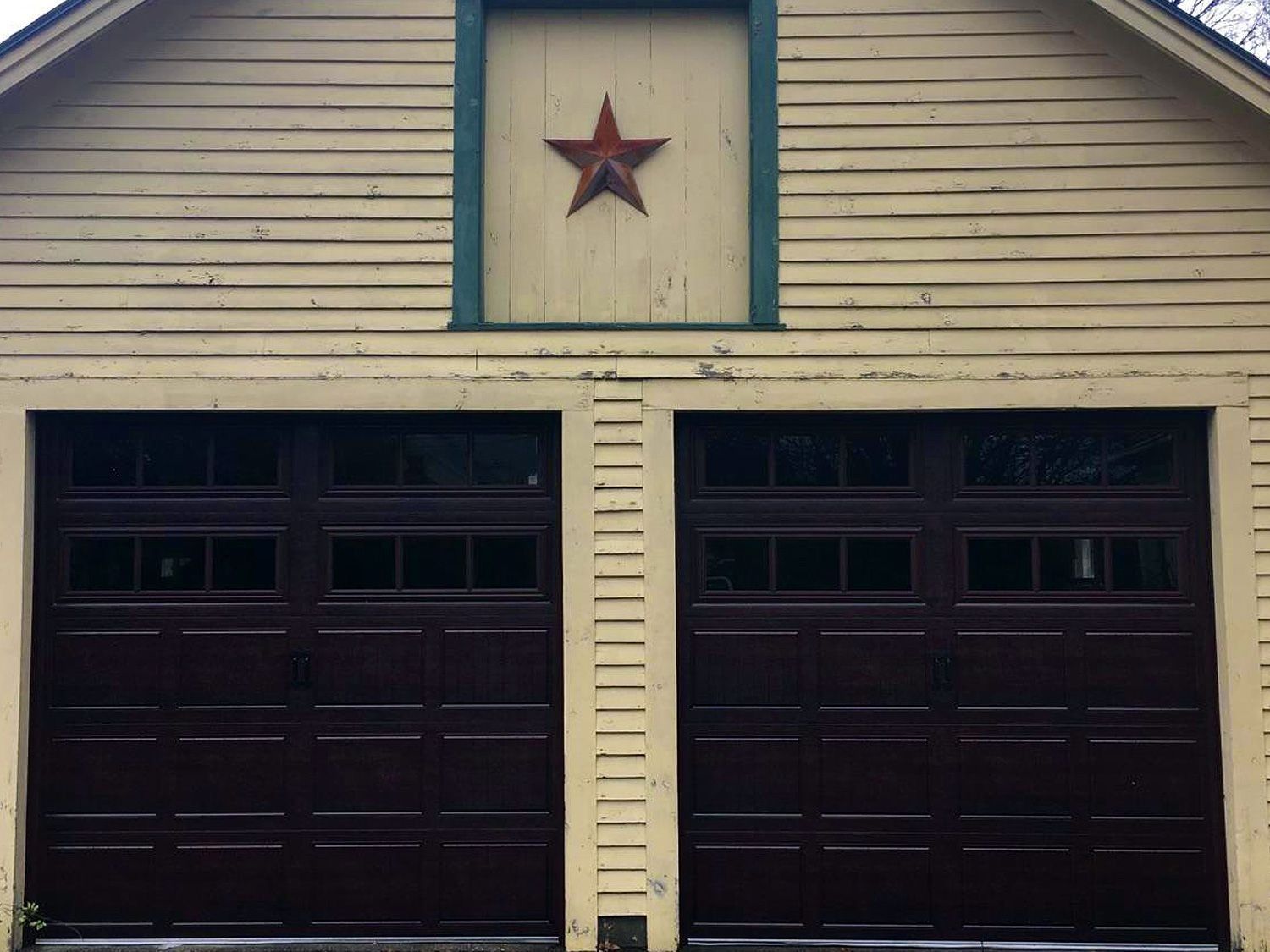 Two dark garage doors beneath beige siding, with a red star centered above them.