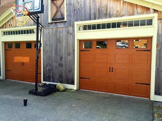 Two orange garage doors on a house with wooden siding and a basketball hoop above one garage.