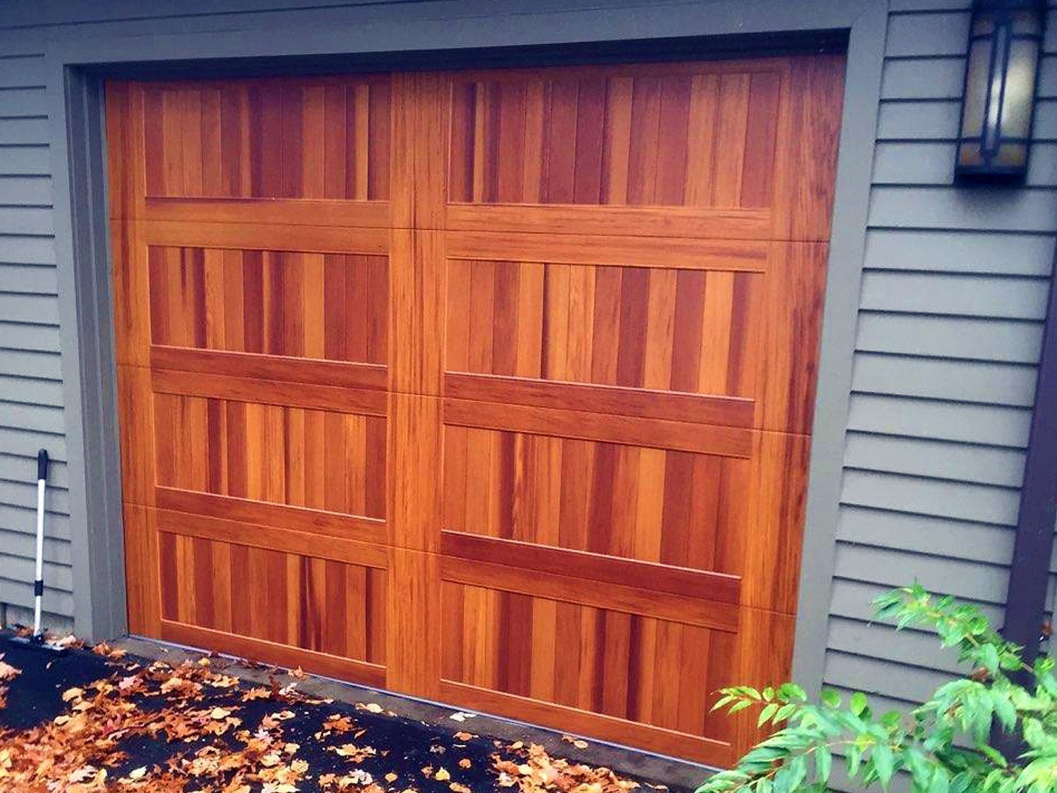 Wooden double garage doors on a gray house with autumn leaves on the ground