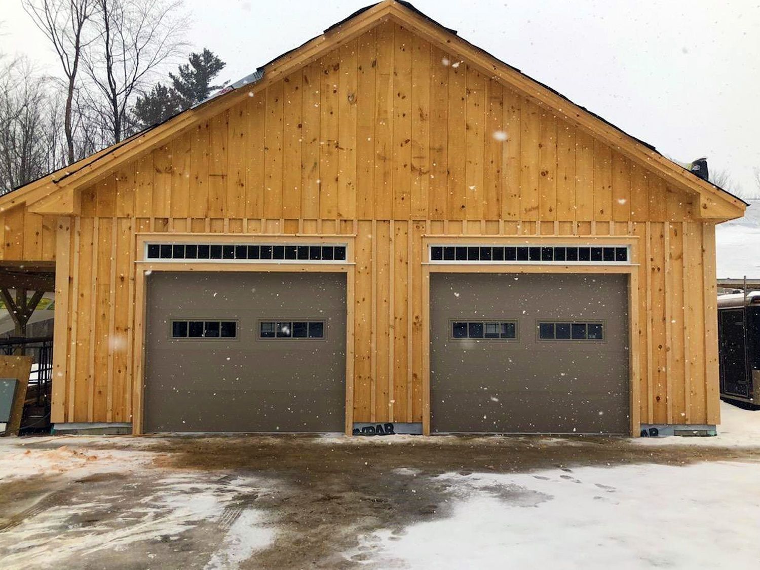 Two-car wooden garage with tan siding and gray doors on a snowy driveway