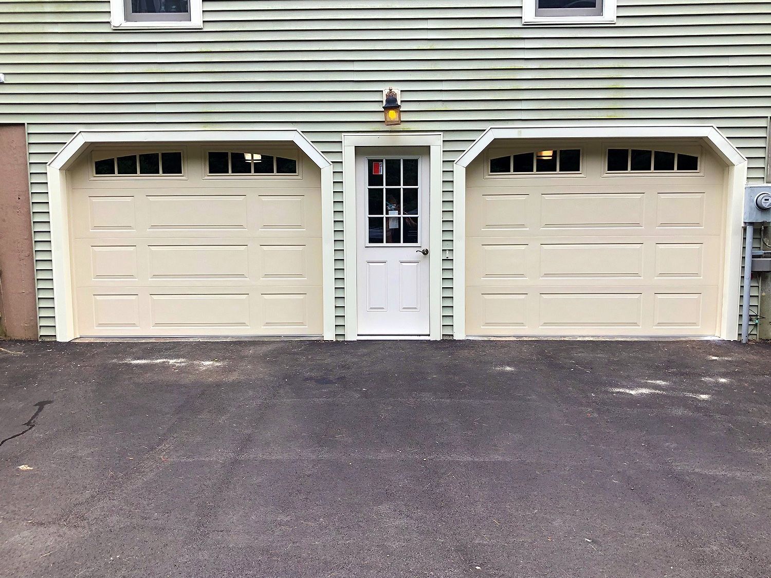 Front view of a two-car garage with beige doors and a white side entry door in a suburban house