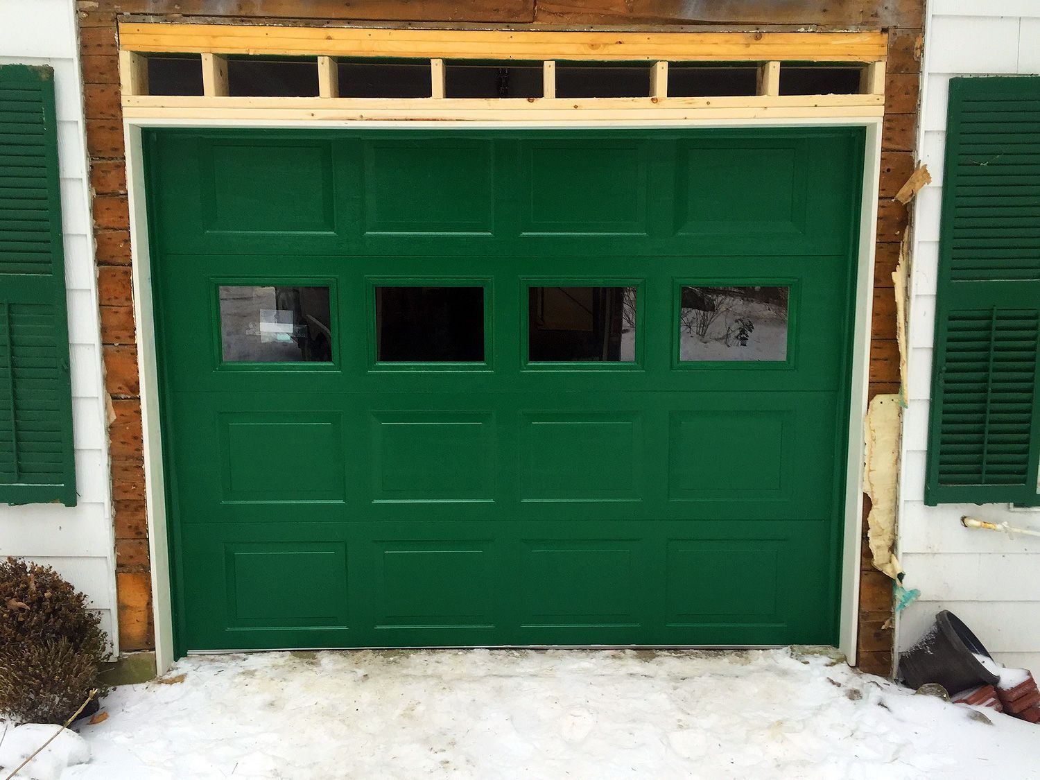 Green garage door with small windows set in a white brick house exterior