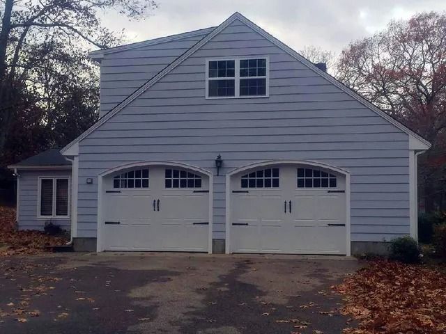 Two-car garage with white siding and arched doors, front view in a wooded yard