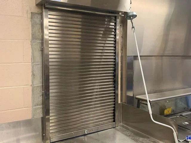 Stainless steel industrial roll-up door in a commercial kitchen with beige tile walls and sink area