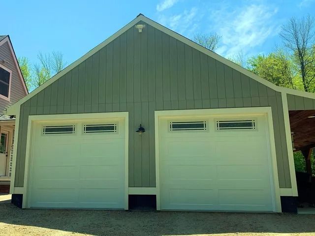 White two-car garage with green siding and garage doors under a gabled roof in daylight