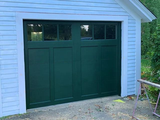 Green garage door on a white-sided house with small windows at the top.