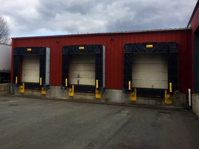 Three white loading dock doors on a red warehouse building under an overcast sky