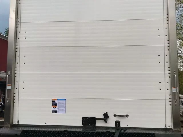 White truck trailer rear door with black latch hardware and a small label near the bottom.