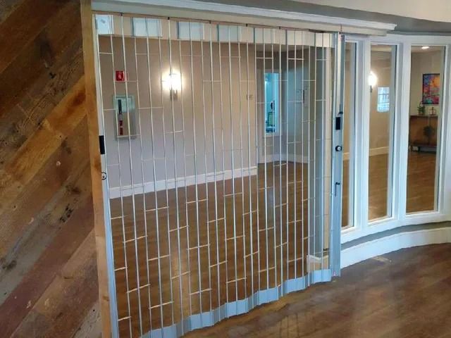 Indoor storefront with a closed white security gate and glass doors in a wood-paneled hallway