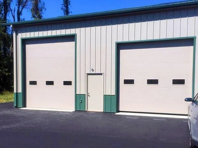 Two white garage doors on a beige metal building with green trim