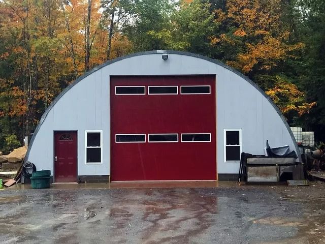 White arched garage with red doors and autumn trees in the background
