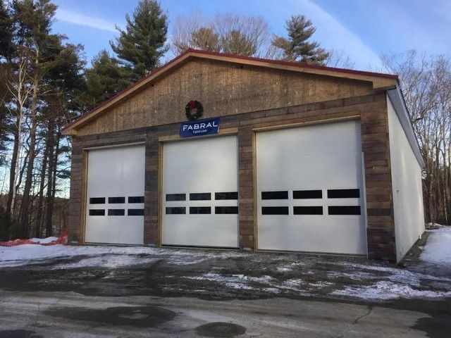 Three-bay garage with white doors and a brown wooden facade in a snowy yard
