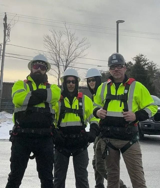 Four cyclists in neon safety jackets and helmets standing together outdoors on a cloudy day.