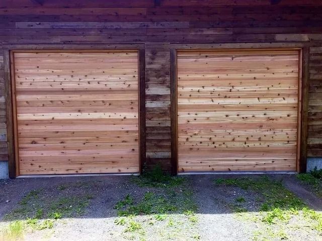 Two wooden garage doors with vertical planks on a brick wall, with grass in front