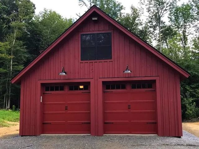 Red two-bay garage with a steep gabled roof and trees in the background