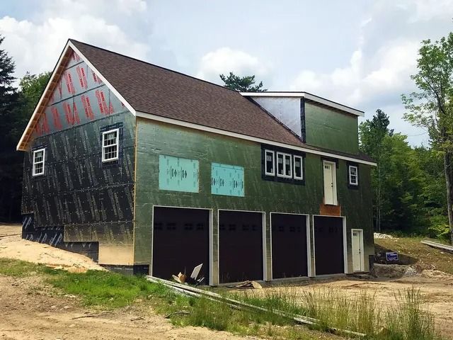 Rustic black-and-green barn with open garage bays beside a dirt path and trees.