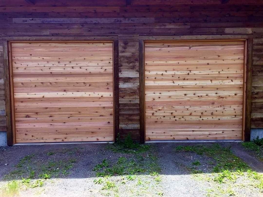 Two wooden garage doors set into a stone wall, with a narrow center pillar and grass in front.