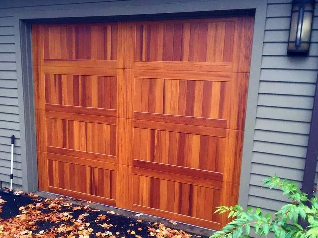 Wooden double garage door with vertical slats on a house exterior, surrounded by gray siding and fallen leaves.