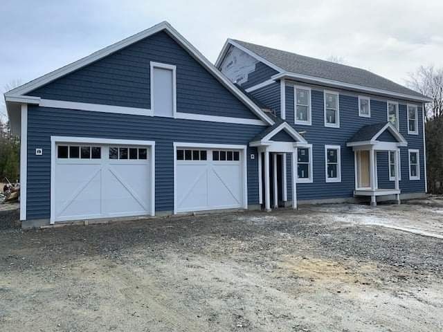 Blue two-story house with white trim and two white garage doors on a gravel driveway