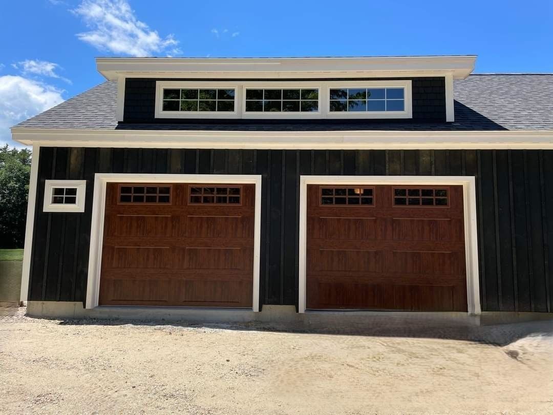 Black garage with two wooden doors and small upper windows under a blue sky