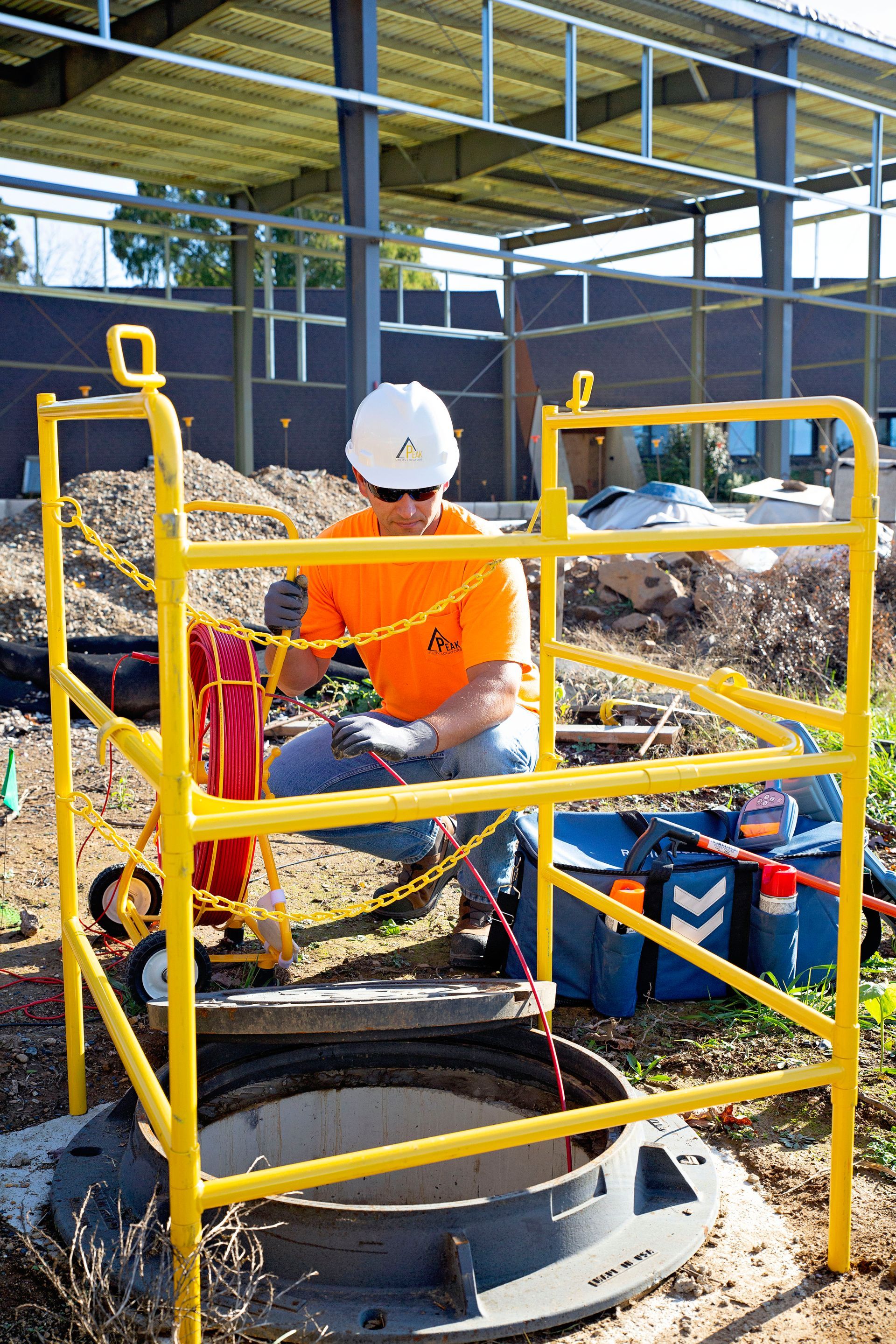 Worker in orange shirt and white hard hat operating machinery behind yellow safety rails at a construction site