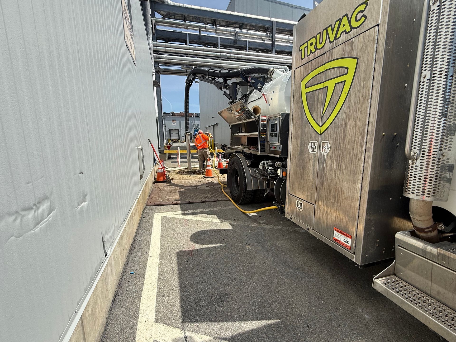 Workers near a TRUVAC vacuum truck in a narrow industrial alley beside a metal building