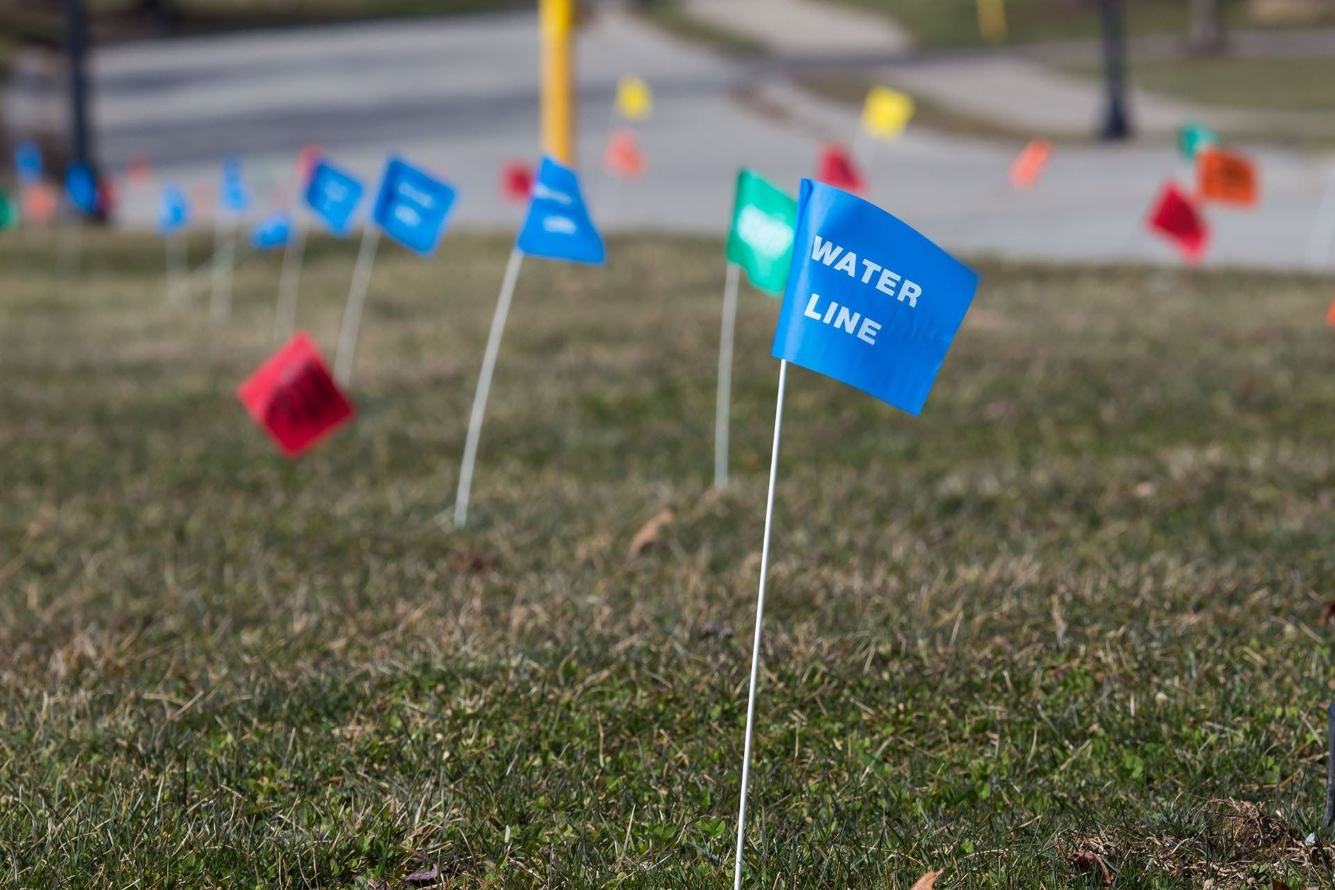 Colorful utility flags marked in a grassy field, including a blue flag labeled “WATER LINE.”