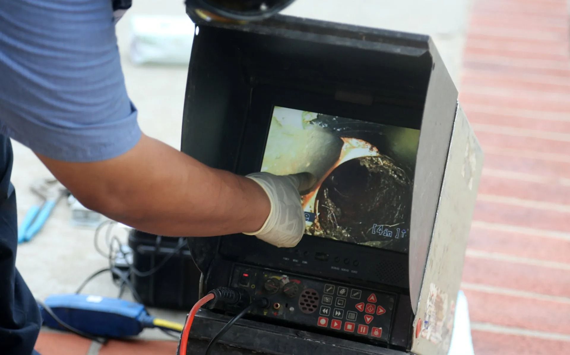 Gloved hand inside a black machine, working on a circular metal part with red cables below