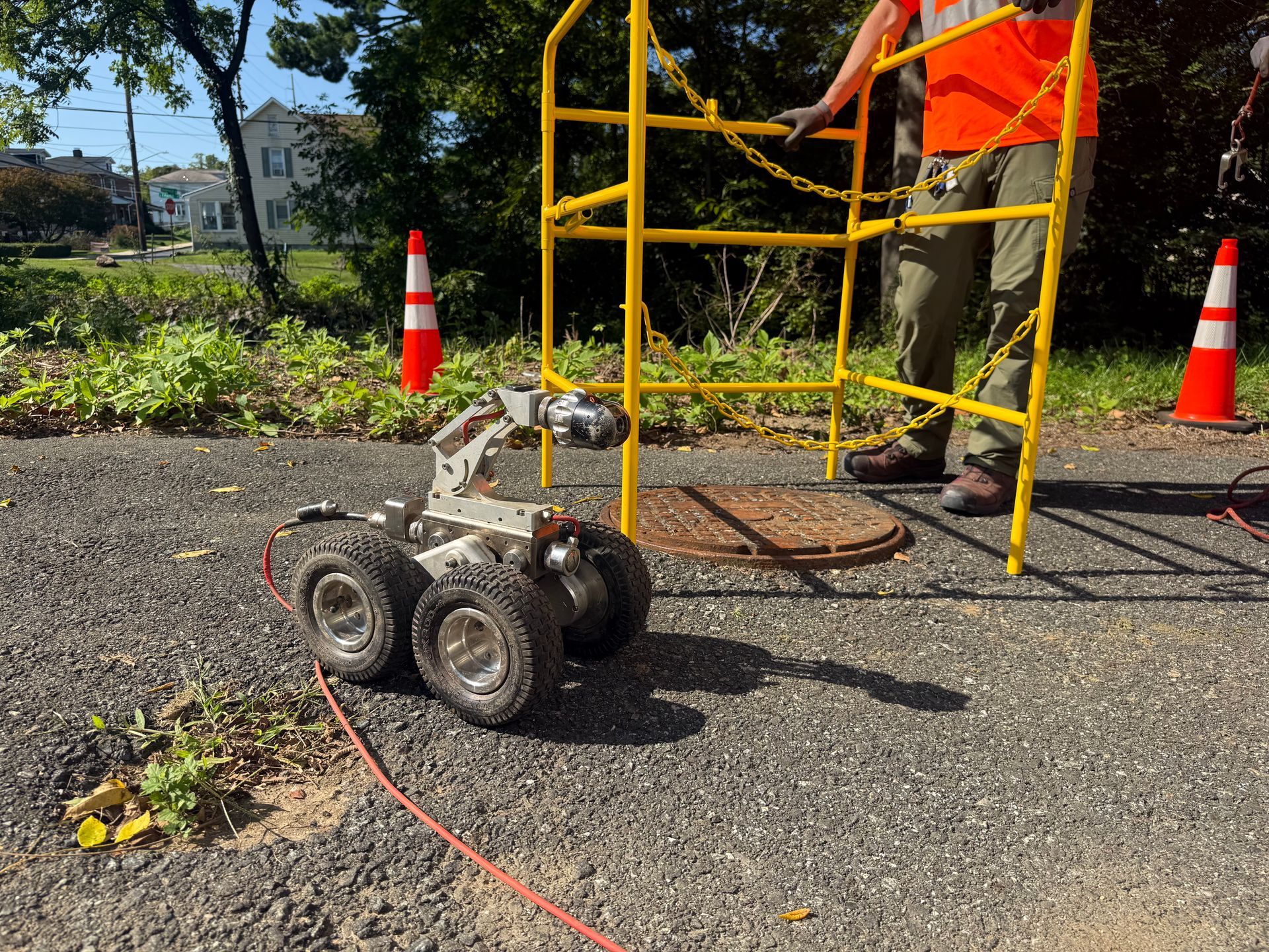 Small tracked robot on gravel beside orange-and-yellow construction scaffolding and traffic cones.