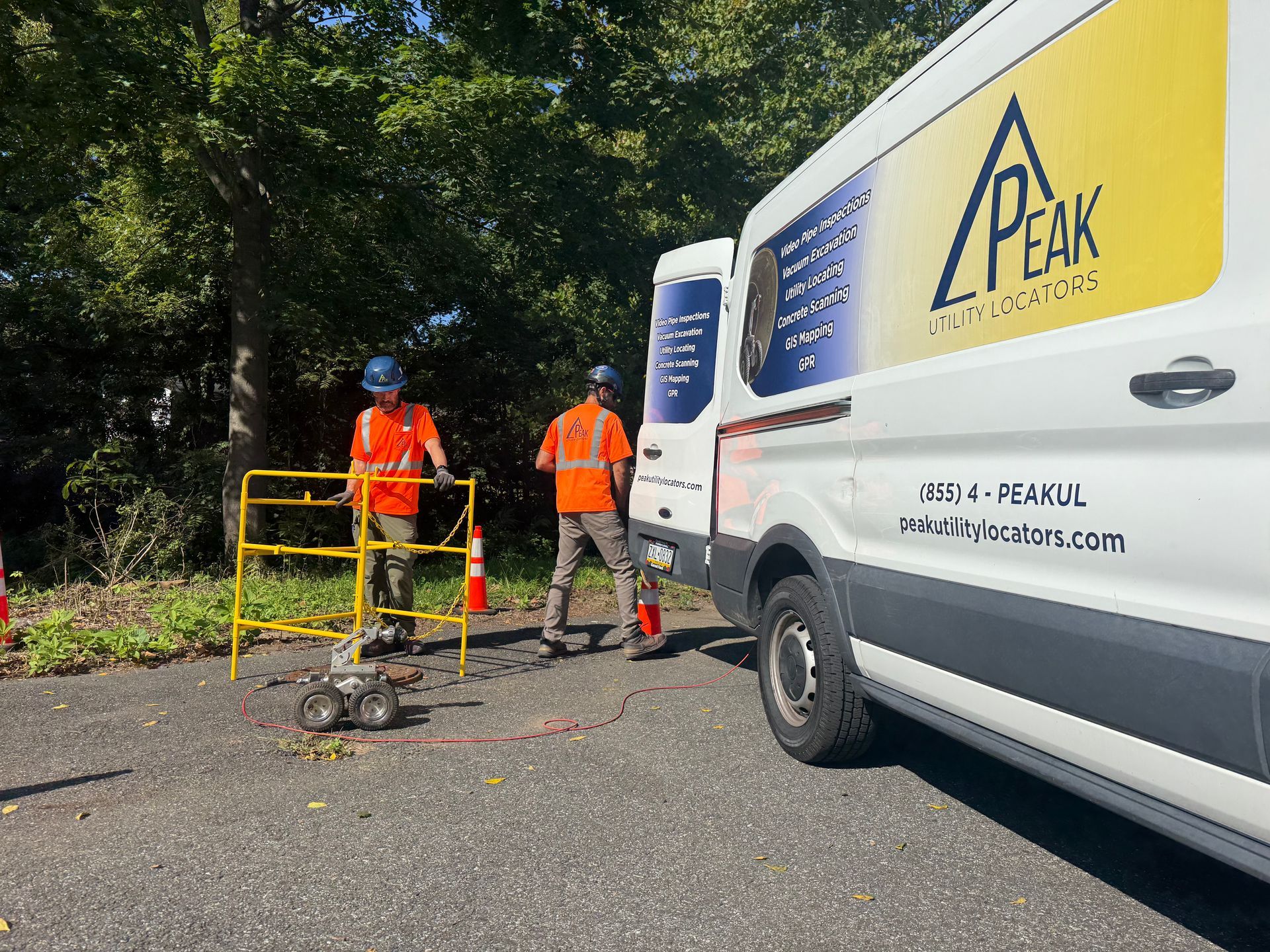 Two workers in orange vests by a white service van on a tree-lined road
