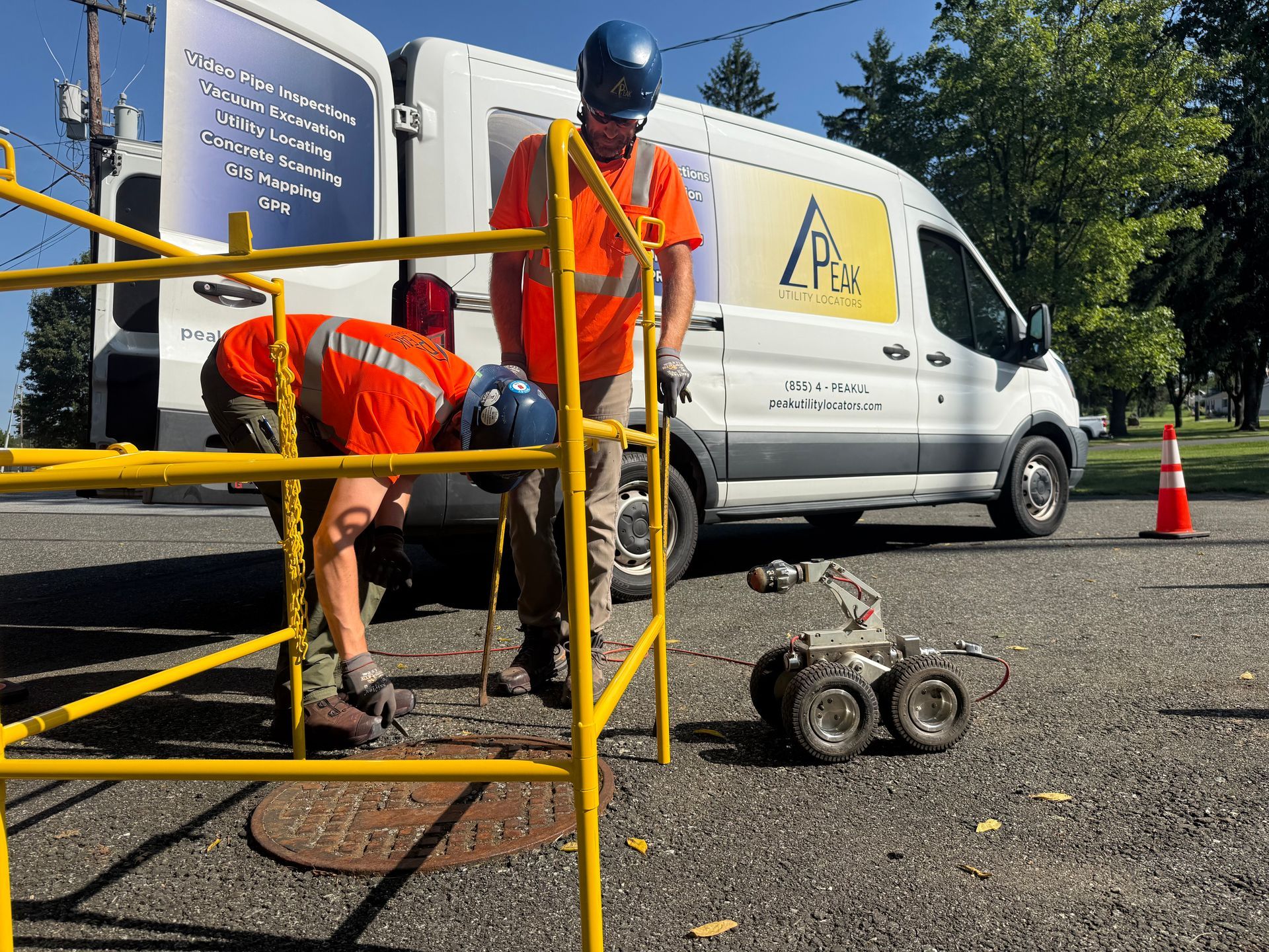 Workers in orange vests and a utility van near a manhole on a street, using equipment and barricades.