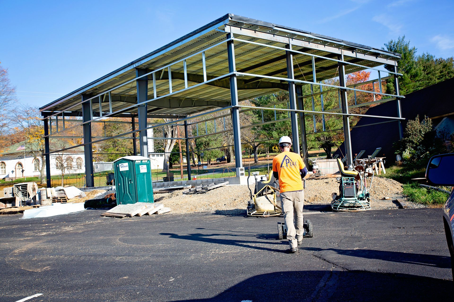 Steel-frame building under construction with workers and equipment on a paved site