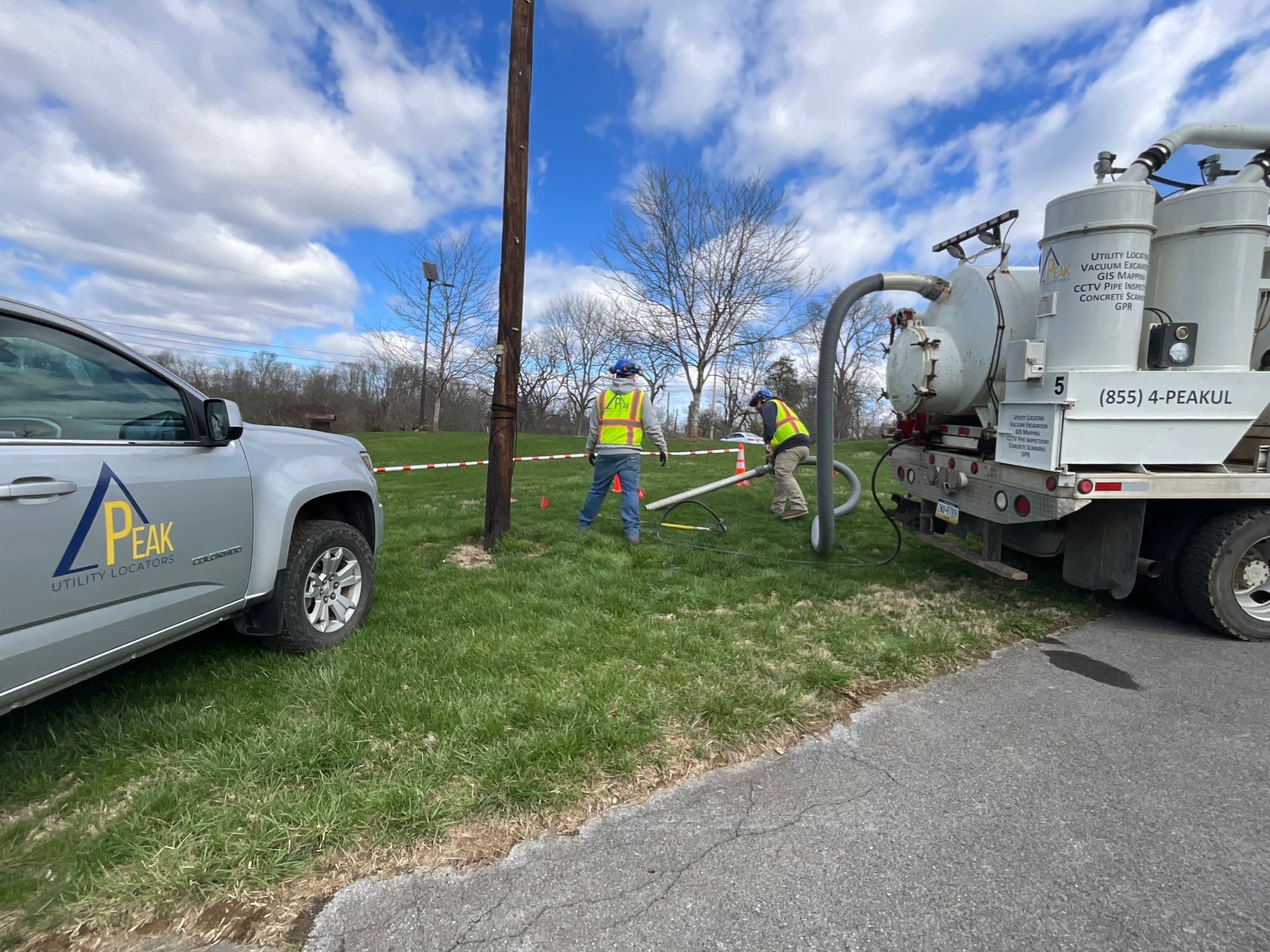 Utility workers and a service truck by roadside equipment under a cloudy sky
