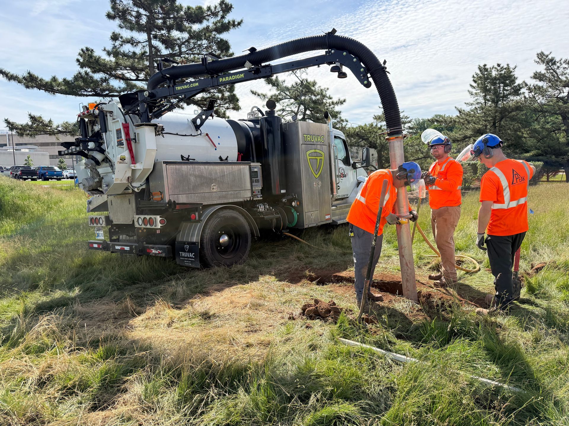 Workers in orange vests inspect a utility truck with hoses in a grassy field